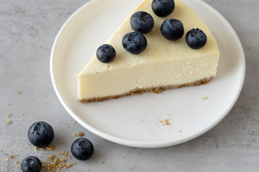 Slice of classic New York cheesecake with graham cracker crust topped with fresh blueberries