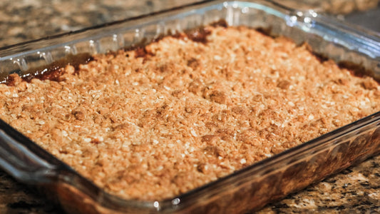 Fresh peach crisp with a golden Jaca oat crumble topping in a glass baking dish